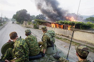Russian soldiers on top of an APC pass by a burning house on the way to Tskhinvali, capital of Georgian 